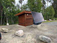 Ferdig SoWin kraftstasjon med solcellepanel montert på betongsockel ved et trehytte