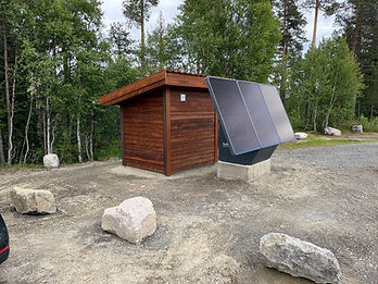 Ferdig SoWin kraftstasjon med solcellepanel montert på betongsockel ved et trehytte