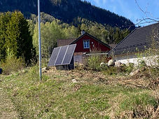 SoWin kraftstasjon med tre solcellepanel på treramme ved rødt hus og trehytte
