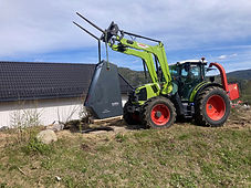 Grønn Claas-traktor løfter en SoWin Kraftstasjon med frontlastar på en gresskledd ås