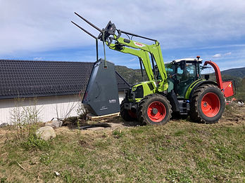 Grønn Claas-traktor løfter en SoWin Kraftstasjon med frontlastar på en gresskledd ås