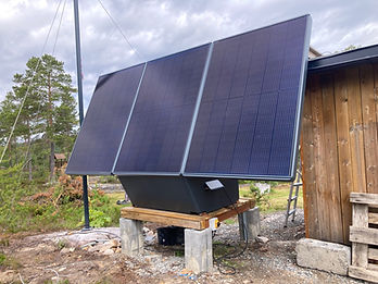 SoWin kraftstasjon med tre solcellepanel på treplattform på betongblokker ved trehytte