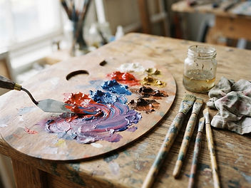 Artist's palette with red and blue oil paint being blended into purple with a palette knife
