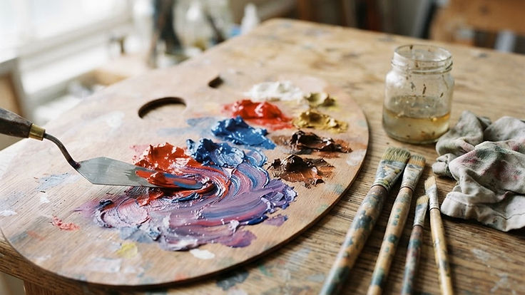 Artist's palette with red and blue oil paint being blended into purple with a palette knife