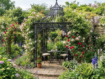 Black metal garden pagoda over a patio bistro set surrounded by climbing roses