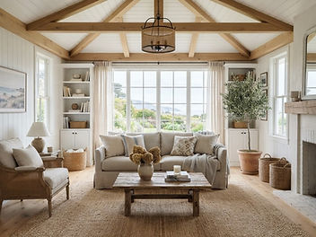 Living room with a white painted tongue and groove timber ceiling and exposed beams, pale walls, a linen sofa, large windows and a light oak floor with an airy coastal country feel