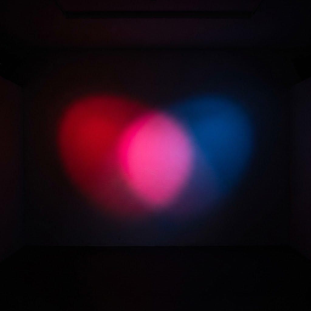 Red and blue spotlights overlapping on a white wall in a dark room, creating a bright magenta pink where the two beams overlap