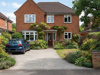 Red brick house with a grey block-paved driveway edged with planted borders