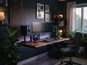 Gaming room with charcoal walls, acoustic slat panels, a wooden desk with a monitor and speakers, an ergonomic chair, purple LED lighting and plants