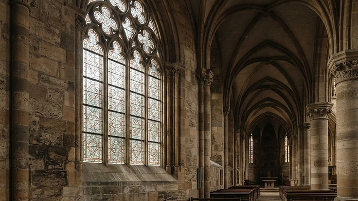 Tall pointed-arch window with stone tracery in a vaulted Gothic church interior
