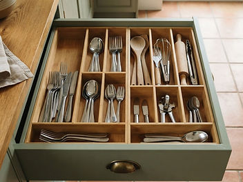 Open kitchen drawer in a sage green kitchen neatly organised with bamboo drawer dividers holding cutlery, wooden spoons, a whisk and other utensils in separate compartments