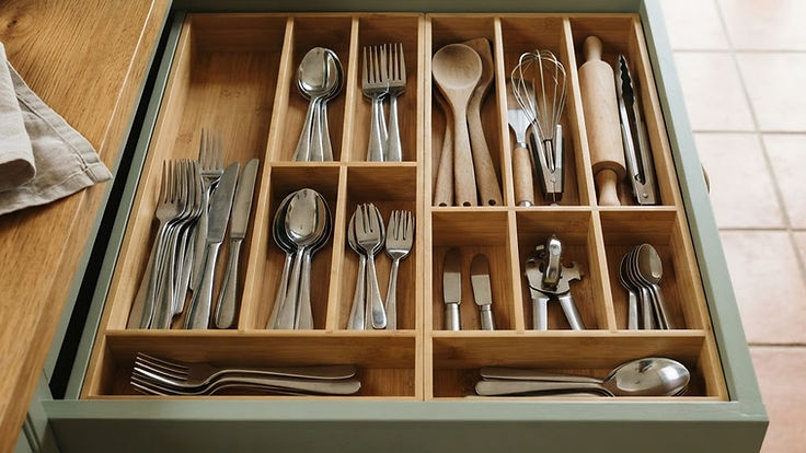 Open kitchen drawer in a sage green kitchen neatly organised with bamboo drawer dividers holding cutlery, wooden spoons, a whisk and other utensils in separate compartments