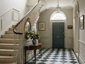 Georgian entrance hall with a black and white chequerboard marble floor, panelled stone coloured walls, a fanlight above a dark front door, a hall lantern and a staircase with slim balusters and a mahogany handrail