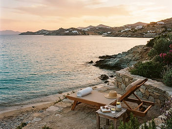 Wooden sun lounger with a straw hat on a rocky Mediterranean terrace overlooking a calm bay at sunset