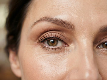 Close-up of a woman's hooded eye with soft matte warm brown eyeshadow blended above the crease, curled lashes with mascara and a softly groomed, lifted brow
