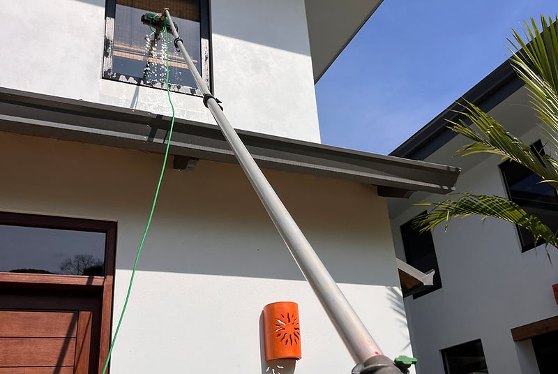 Professional window cleaner using a water-fed pole on a tropical home