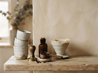 Coffee tools and stacked handmade ceramic cups on a pale oak shelf