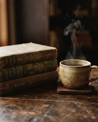 A stack of vintage books beside a ceramic coffee cup on dark timber