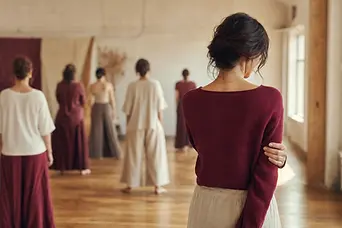Grup de participanți estompați într-o sală de atelier, cu o femeie care se retrage spre fereastră.