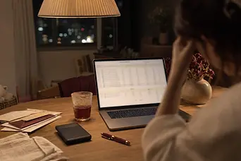 Laptop cu bugetul familiei, plicuri și o cană de ceai rece pe masa din sufragerie, noaptea.