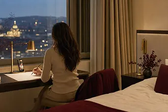 Femeie într-o cameră de hotel, seara, desenând linii simple pe o coală, în delegație.