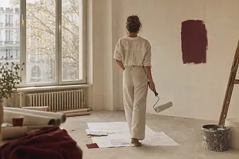 Femeie cu un trafalet într-un apartament în renovare, cu planuri întinse pe podea.
