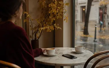 Femeie într-o cafenea modernă din București, cu telefonul pe masă și o ceașcă neatinsă în față.