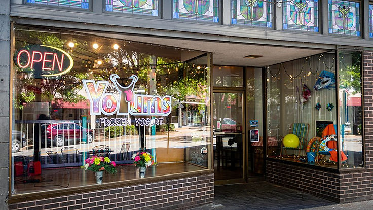 The YoYums storefront on East High Street: a dark brick base, stained-glass panels above the windows, and the YoYums Frozen Yogurt sign centred in the glass.