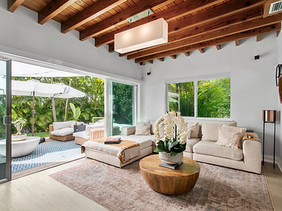 Open living room with exposed wood beams and a sectional sofa, sliding glass doors open to a garden patio at 434 Loretto Avenue