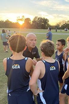 A coach talking with the GCA cross country team at sunset