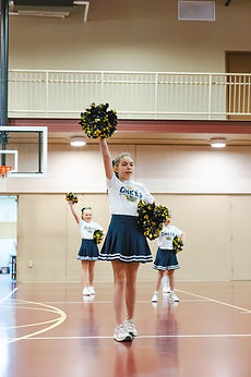 A GCA cheerleader raising her pom-pom in the gym