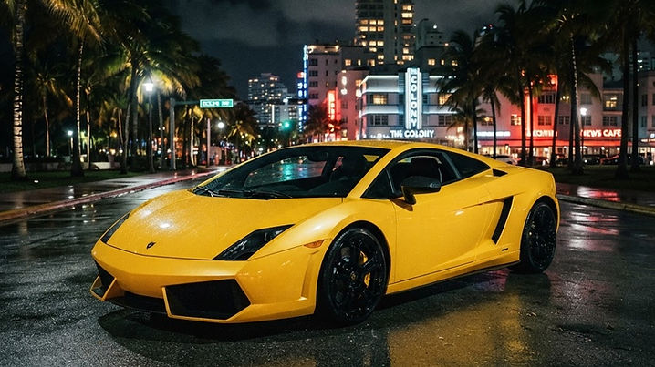 A bright yellow Lamborghini Gallardo parked at night on a wet palm-lined boulevard in Miami