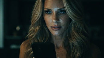 Close-up of Paige's anxious face lit only by the cold glow of her smartphone in a pitch-dark condo