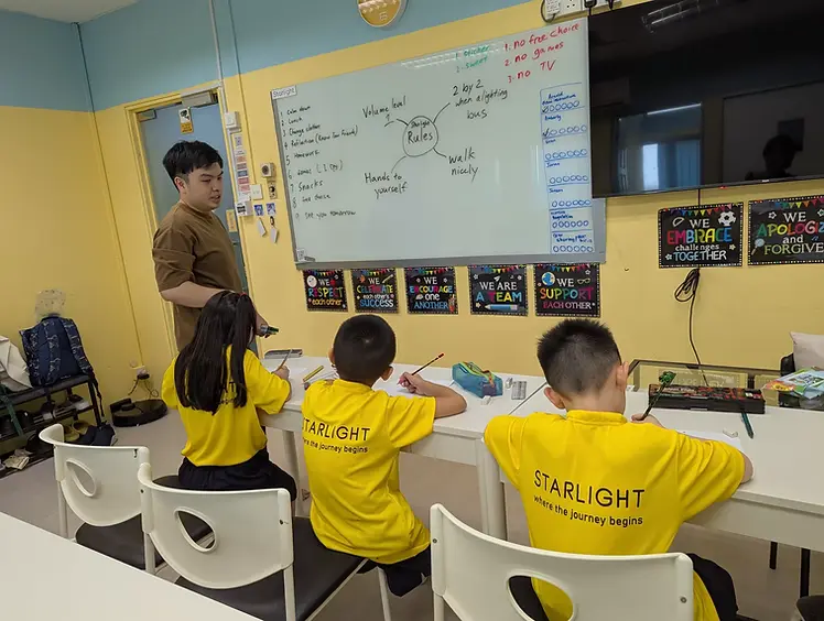 Starlight Centre teacher reviewing the Starlight Rules whiteboard with students in yellow uniforms