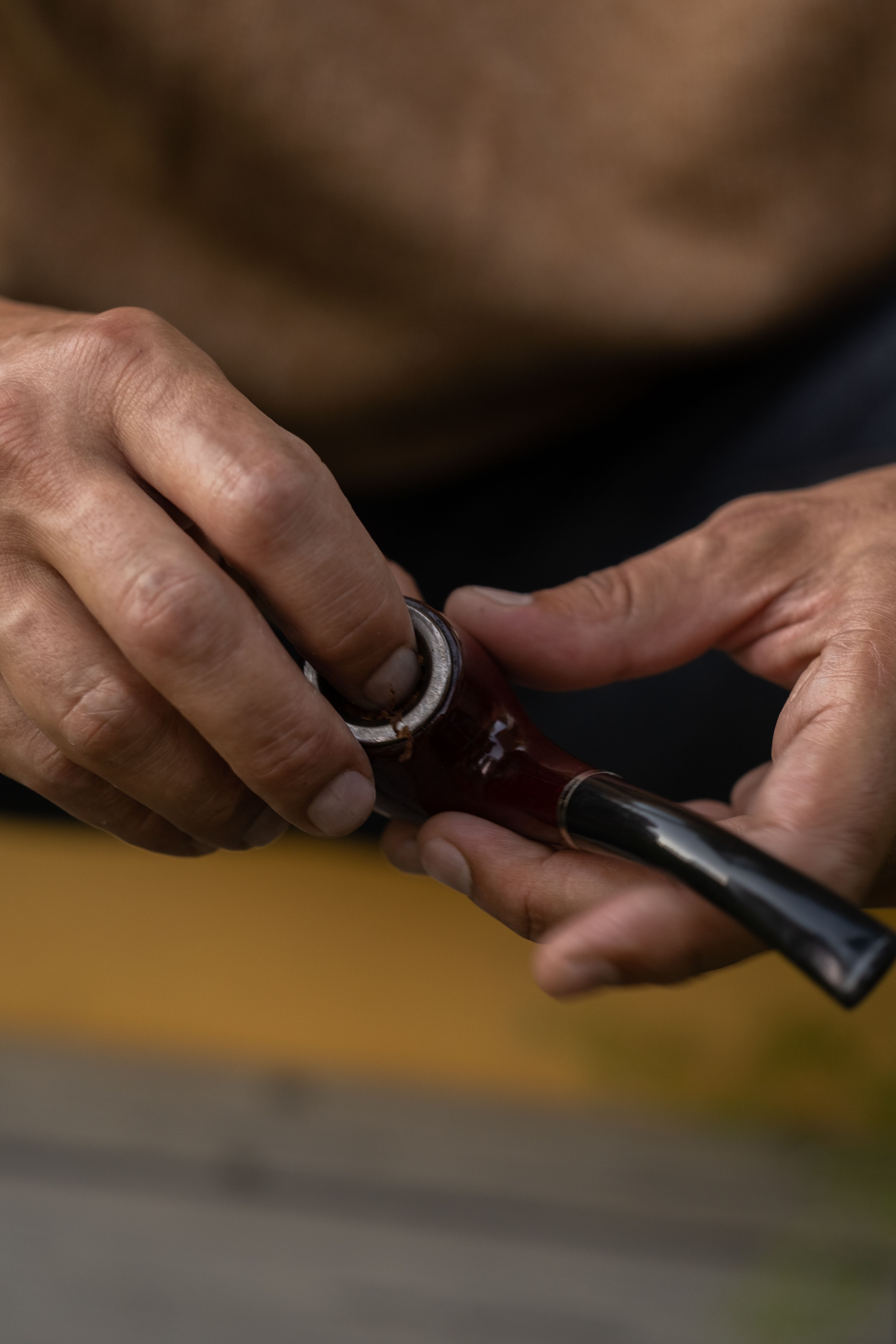 Hands pressing pipe tobacco into the bowl of a dark mahogany pipe