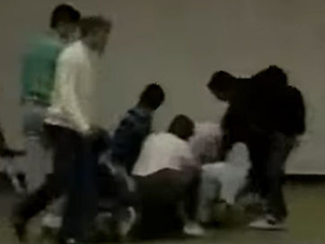 A grainy footage still: several people leaning over and holding a person down on the floor
