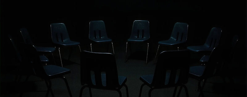A circle of empty chairs under a single overhead light