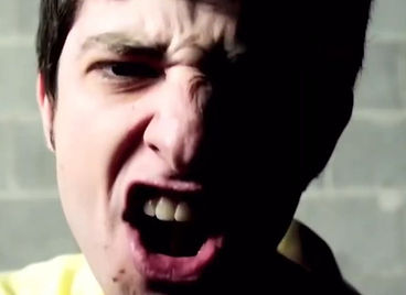 A close-up of a young man screaming, one side of his face in shadow, against a concrete block wall