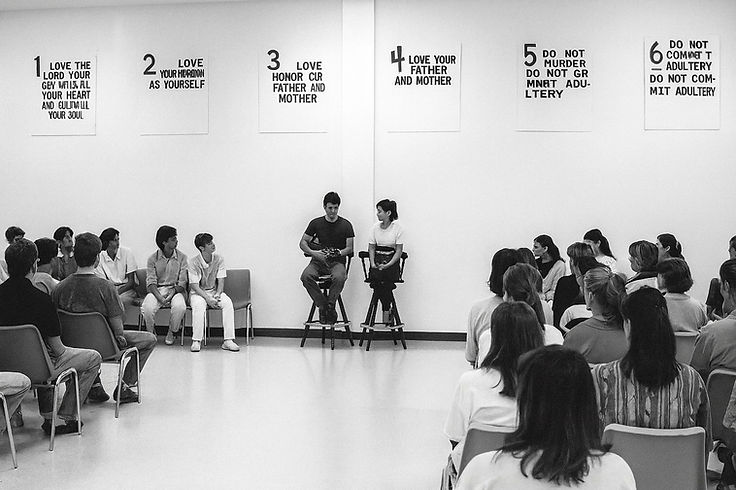 The group seated in a semi-circle facing two clients on stools, the numbered rules posted along the wall