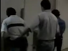 The same escort in footage, a hand hooked through the back of the trousers of the client ahead