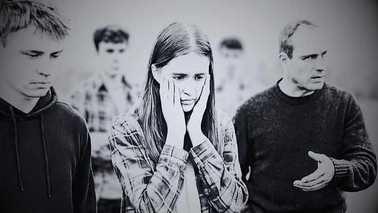 A night portrait of a distressed young woman holding her cheeks, an older man mid-lecture beside her and other faces behind