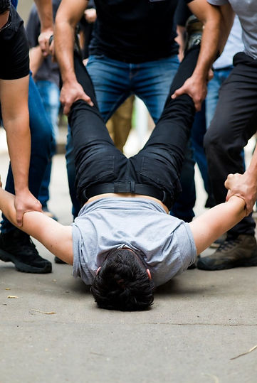 A person held face-down on a concrete floor, arms pinned out to either side and legs lifted by others