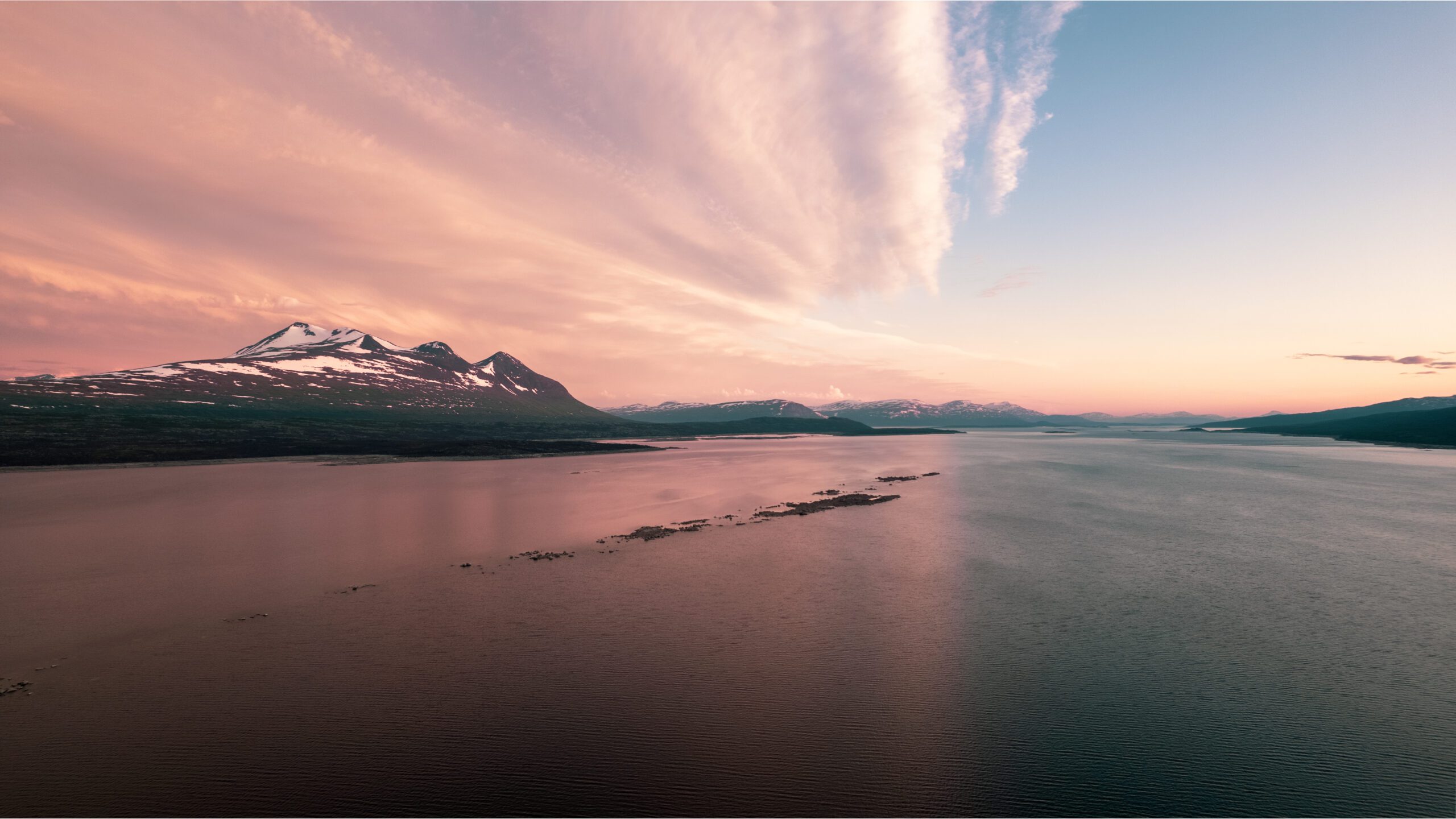 Vandrare med ryggsäck på plankstig genom lappländsk tundra mot snötäckta fjäll