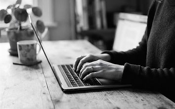 Black and white photo of hands typing on a laptop at a kitchen table
