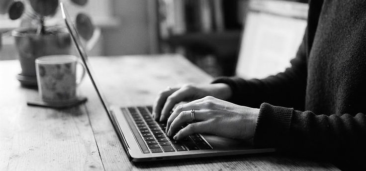 Black and white photo of hands typing on a laptop at a kitchen table