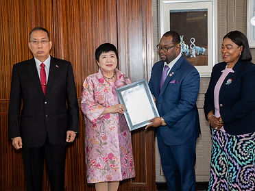 A certificate being handed to a delegate in a pink patterned jacket while officials look on