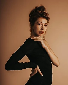 Waist-up portrait of a model in a black one-shoulder dress against a muted beige background