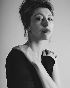 Black and white studio portrait of a woman in a black one-shoulder top with hands on her shoulders