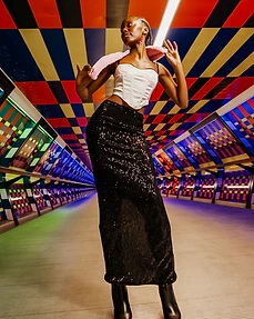 Full-body shot of a model in a white corset and black sequin skirt standing in a futuristic coloured-panel walkway