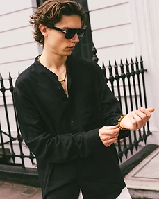 Male model in a black shirt adjusting a beaded bracelet against a white panelled wall
